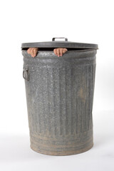 A classic metal garbage can with only the fingers showing of someone that is hading inside.