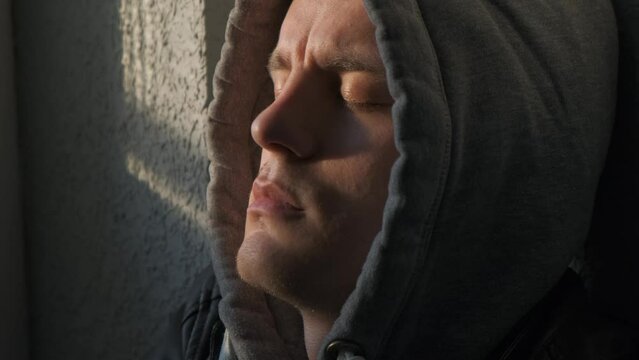 Young man with sadness on his face leaning his head against the wall, close-up