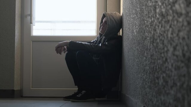 Thoughtful sad man in a hood thinks about something leaning against the wall