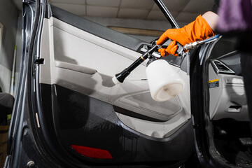 Cleaner is washing car door card panel and spraying detergent from tornador gun. Car detailing with tornador cleaning gun with high pressure air pulse.