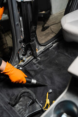 Fototapeta na wymiar Close-up vacuum cleaning of dirty car floor with removed seats in detailing service. Worker of detailing service is using vacuum cleaner for remove dust and dirt in car.