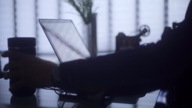A freelancer man typing on a laptop keyboard and sipping coffee
