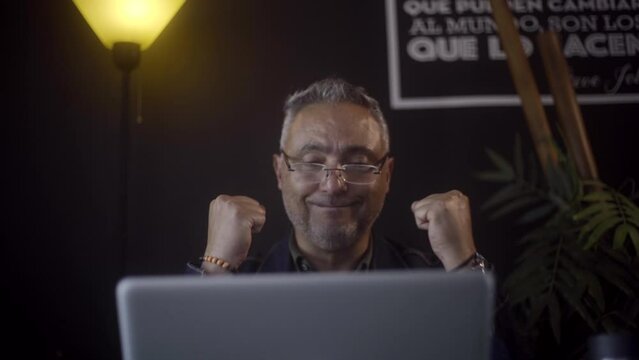 Freelancer man jumping with excitement in front of his screen fter receiving good news on his laptop.