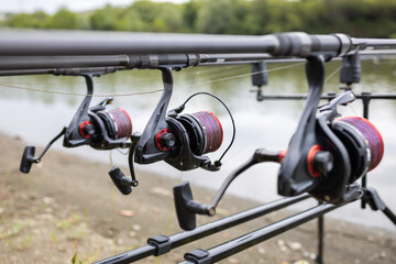 Three rods with reels on stand ready for carp fishing in a beautiful lake. Spools of coiled purple line close up.