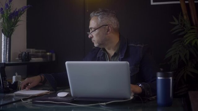 Male freelancer typing and writing on his laptop in his personal workspace.