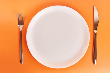 White plate with fork and knife on orange background.