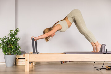 Woman training pilates on the reformer bed. Reformer pilates studio machine for fitness workouts in...