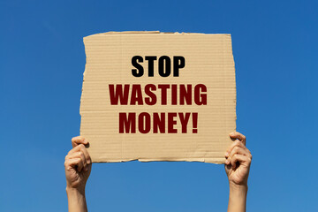 Stop wasting money text on box paper held by 2 hands with isolated blue sky background. This...