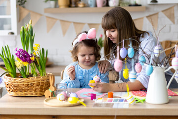 Beautiful mother and cute daughter are spending quality time together, making craft handmade eggs for Easter home decoration. Spring flowers, cozy holiday atmosphere , family traditions and values