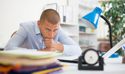 Tired office worker with displeasure looks at pile of documents on the table