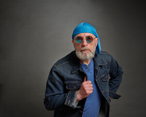 portrait of senior, confident, handsome man with gray beard in skull cap and trucker jacket wearing round blue sunglasses