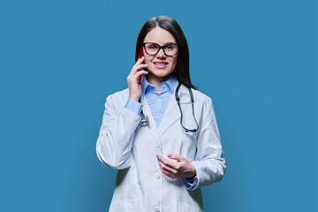 Young female doctor talking on mobile phone, on blue background