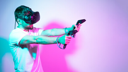Bearded man in VR glasses plays in simulation figth and using controllers in in multicolored neon...