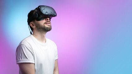 Bearded man in VR glasses communicates with a friends in a metaverse and looking up. Neon background. Enjoying Modern Augmented reality, and meta, concept virtual space in future. Mock up. Copy space