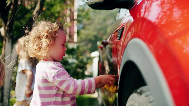 Adorable little girl washes a red car in the garden