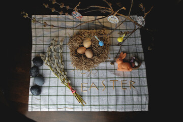 Original Easter decorations. Nest with eggs, rabbit and willow branches. Space for text. Easter concept in dark colors.

