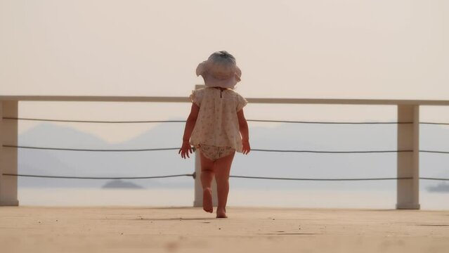 Baby girl runs towards sea on the seaside jetty, slow motion. New horizon or discovery concepts