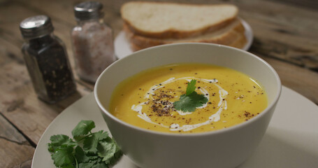 Close up of white bowl of carrot soup with bread and carrots on wooden background