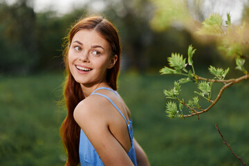 Naklejka na ściany i meble Portrait of a young woman with a beautiful smile with teeth in nature on the background of trees in the spring on a sunny day, the beauty of health and youth, happiness, freedom