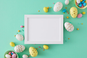 Easter concept. Flat lay photo of colorful easter eggs and sprinkles on teal background and white photo frame in the middle. Holiday card idea