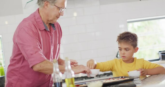 Happy caucasian grandfather and grandson making pizza in kitchen, slow motion