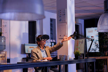 Executive manager wearing virtual reality goggles, analyzing marketing statistics hologram. Businesswoman working late at night at company strategy in startup office. Corporate concept