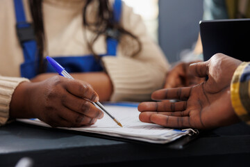 African american delivery service worker searching parcel code in clipboard. Postal warehouse employees checking goods inventory documentation and taking notes hands close up