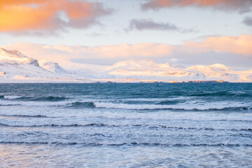 Scenic Winter Atlantic Ocean Coast at Sunset. Snow Covered Mountains in Iceland. Icelandic Fjords During Stormy Weather. Clouds Illuminated by the Warm Rays of the Sun.