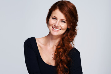 Stylish strands. Studio shot of a young woman with beautiful red hair posing against a gray...