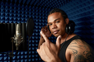 Close-up of an afro american rap artist with headphones while recording a song at a recording studio