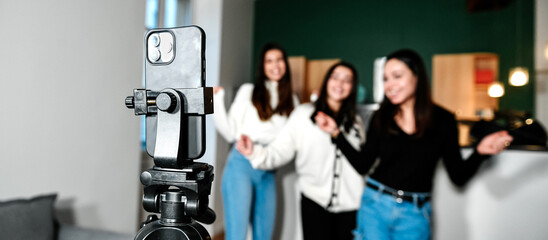 Close-up of a smartphone on a tripod filming 3 young white girls dancing, at home. Concept of...