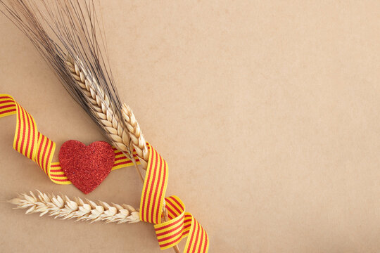 Sant Jordi. fondo celebraci&oacute;n festividad catalana, con tres espigas de trigo, una cinta con la bandera de catalu&ntilde;a y un coraz&oacute;n de purpurina color rojo. diada de catalu&ntilde;a