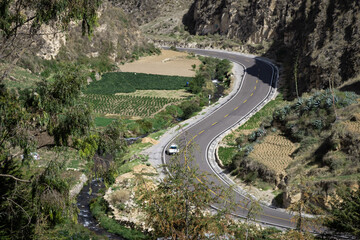 Carretera entre colinas recorre el valle al lado de un rio, día soleado