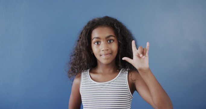 Happy african american girl using sign language on blue background, slow motion