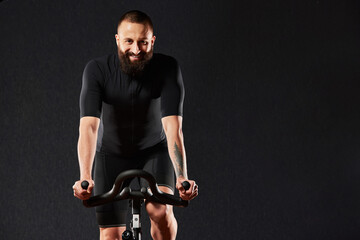 Man smiling on exercise bike copyspace dark background, man doing cardio workout on exercise bike,...