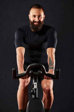 Man smiling on exercise bike dark background, man doing cardio workout on exercise bike, fat burning, weight loss, sport lifestyle concept