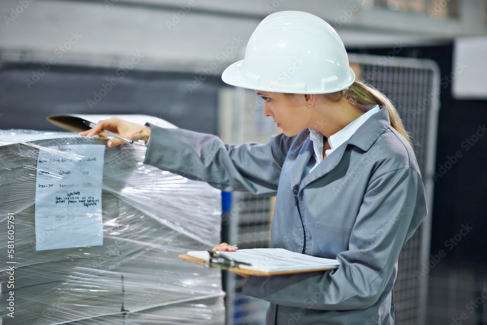 Poster checking its the right batch. a woman wearing a hardhat inspecting inventory in a factory.