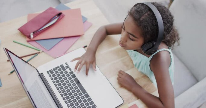 African american girl sitting at table, using laptop for online lesson, slow motion