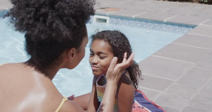 Happy african american mother and daughter applying sunscreen by swimming pool, slow motion