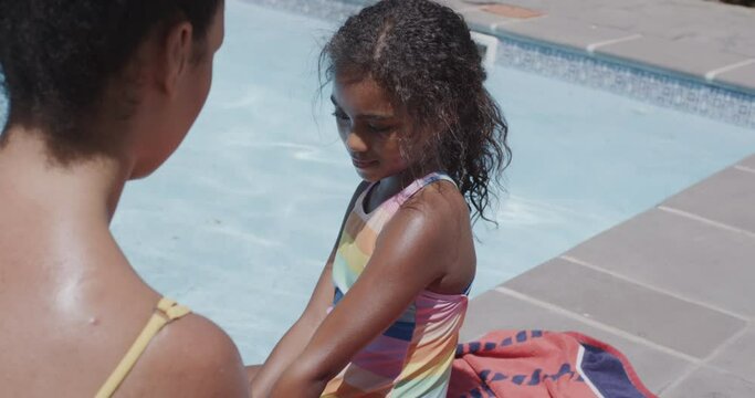 Happy african american mother and daughter applying sunscreen by swimming pool, slow motion