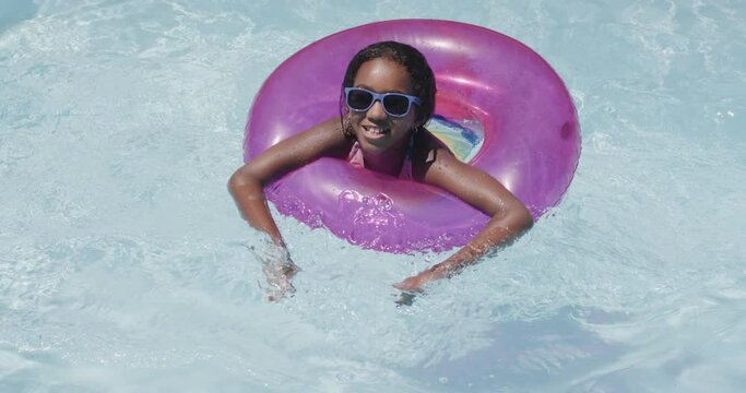 Portrait of happy african american girl using swim ring in swimming pool, slow motion