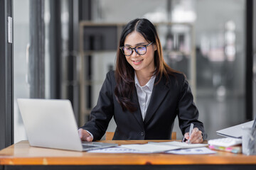 Asian Businesswoman Using laptop computer and working at office with calculator document on desk, doing planning analyzing the financial report, business plan investment, finance analysis concept.
