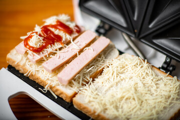 open sandwich maker with cheese toast and sausages. Sandwiching.