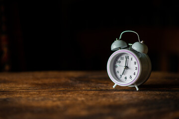 Naklejka premium White alarm clock on a dark wooden background. Place for text. Circadian rhythm, time management.
