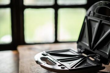 Open empty sandwich maker on the background of an old-fashioned house window. Cooking toast. Place for text.