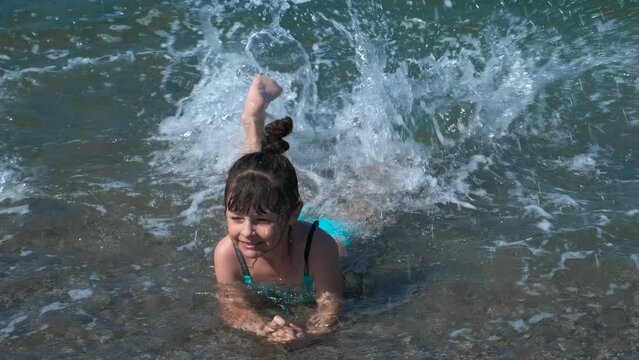 Child making waves on exotic beach. A smiling little girl have a luxury relaxation in the ocean water by the shore.