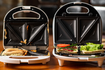 a variety of sandwiches that can be prepared in a sandwich maker concept. Row of electric sandwich makers on a wooden background.