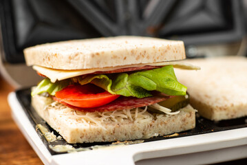 Whole wheat toast sandwich with salami and herbs in a sandwich maker close-up.