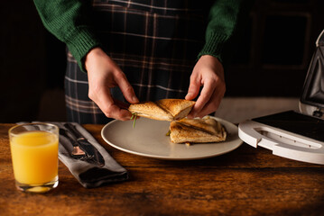 Unrecognizable woman takes a sandwich toast on a wooden background. Morning breakfast, snack, diet.