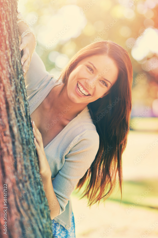 Poster Playful park pottering. a beautiful young woman standing behind a tree at the park.